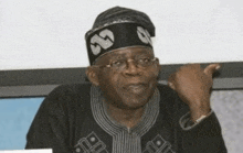 a man wearing glasses and a black hat is sitting in front of a screen .