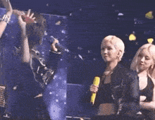 a woman is holding a microphone while standing on a stage with other women .