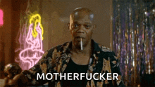 a man is smoking a cigarette in front of a neon sign and the word motherfucker is on the screen .