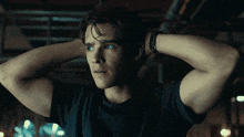 a young man with his hands behind his head looks at the camera