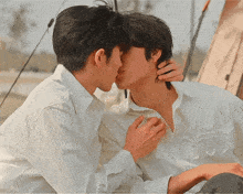 two men in white shirts are kissing each other in front of a tent .