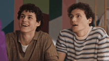 two men with curly hair are sitting next to each other and smiling