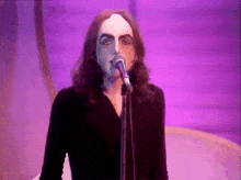 a man with long hair singing into a microphone with a purple background