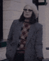 a woman wearing a plaid sweater and a striped jacket stands in front of a building