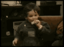 a young boy is sitting on a couch eating a piece of chocolate .