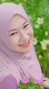 a woman wearing a purple hijab is smiling while holding flowers