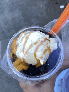 a person is holding a plastic cup of ice cream with caramel sauce