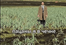 a man in a trench coat and tie is standing in a field with a caption in russian
