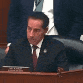 a man in a suit and tie is sitting at a table with a name tag that says mr. raskin