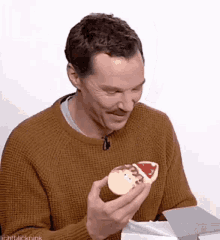 a man in a brown sweater is holding a christmas cookie with a reindeer on it .