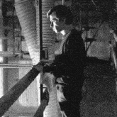 a black and white photo of a man standing on a railing in a factory .