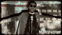 a man wearing sunglasses and a hat is standing in front of a microphone with the words madistation behind him