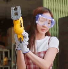a woman wearing safety goggles and gloves is holding a yellow drill
