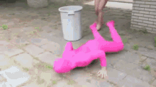 a person in a pink bodysuit is rolling on the ground next to a trash can .