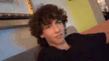 a young man with curly hair is sitting on a couch making a funny face .