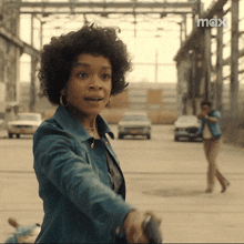 a woman in a blue jacket is holding a gun in a parking lot in front of a max logo