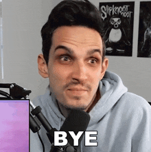 a man in a hoodie stands in front of a microphone with the word bye in front of him