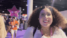 a woman in a white shirt is smiling in front of a pink star balloon
