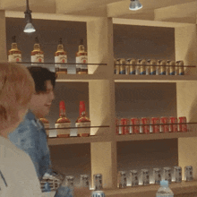 a man stands in front of a shelf full of bottles and cans including a bottle of jim beam