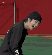 a man wearing a black beanie is laughing while sitting on a green mat .