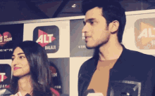 a man and a woman are standing in front of a sign that says alt balaji