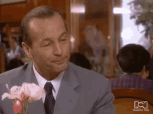 a man in a suit and tie is holding a bouquet of pink roses in front of a nuestra tele sign