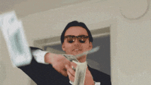 a man in a suit and sunglasses is throwing money into the air .