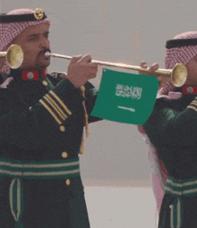 a man playing a trumpet while holding a green flag that says ' saudi arabia ' on it