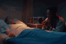 a man sits next to a woman in a hospital bed holding her hand