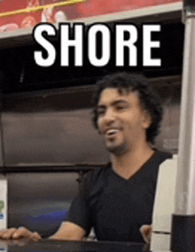 a man is sitting at a counter in a restaurant with a sign that says shore behind him .