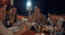 a group of people are sitting at a table with bottles of wine and plates of food .