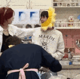 a group of people are standing in a kitchen and one of them is wearing a sunflower headband .