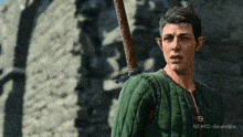 a man in a green jacket is holding a sword on his shoulder .