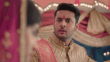 a man with a red bindi on his forehead looks at a woman in a red dress