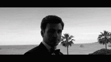 a black and white photo of a man in a tuxedo looking at the ocean .