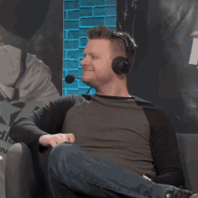 a man wearing headphones sits on a couch in front of a brick wall that says adidas