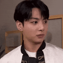 a young man with a piercing in his lip is wearing a white jacket and a black jacket .