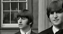 a black and white photo of two men standing next to each other in front of a building .