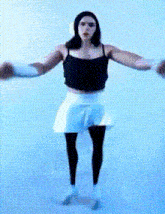 a woman in a black tank top and white skirt is dancing
