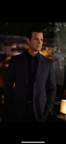 a man in a suit and black shirt is standing in a dark room .