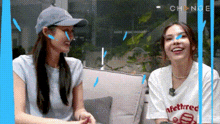 two women are sitting next to each other on a couch laughing .