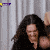 a woman with curly hair is making a funny face in front of a sign that says katseye .