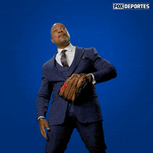 a man in a suit and tie is holding a baseball glove in front of a blue background that says fox deportes on it
