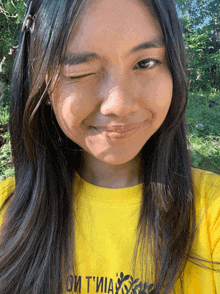 a girl wearing a yellow t-shirt that says " oi tvia " winks at the camera