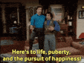 two men standing next to each other in a living room with the words here 's to life puberty and the pursuit of happiness below them