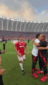 a man in a red aura shirt is hugging another man on a field