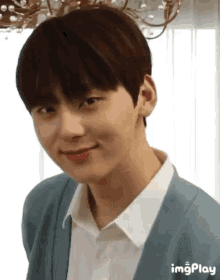 a young man wearing a white shirt and a blue cardigan is smiling .