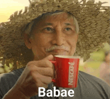 a man wearing a straw hat is drinking a cup of coffee .