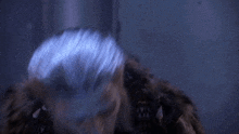 a man with blue hair and a fur coat is standing in the dark .