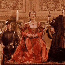 a woman in a red dress is sitting on a throne with two men in armor